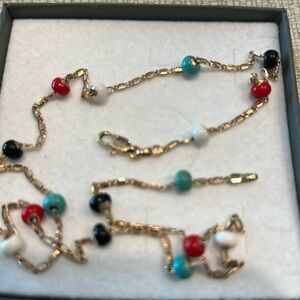 Gold tone necklace with red, blue and black beads spaced along a 18.5” chain.
